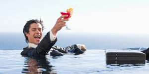 Delighted businessman relaxing in a swimming pool with a cocktai