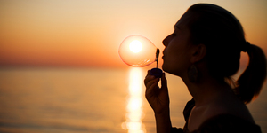 Girl making soap bubbles over sunset